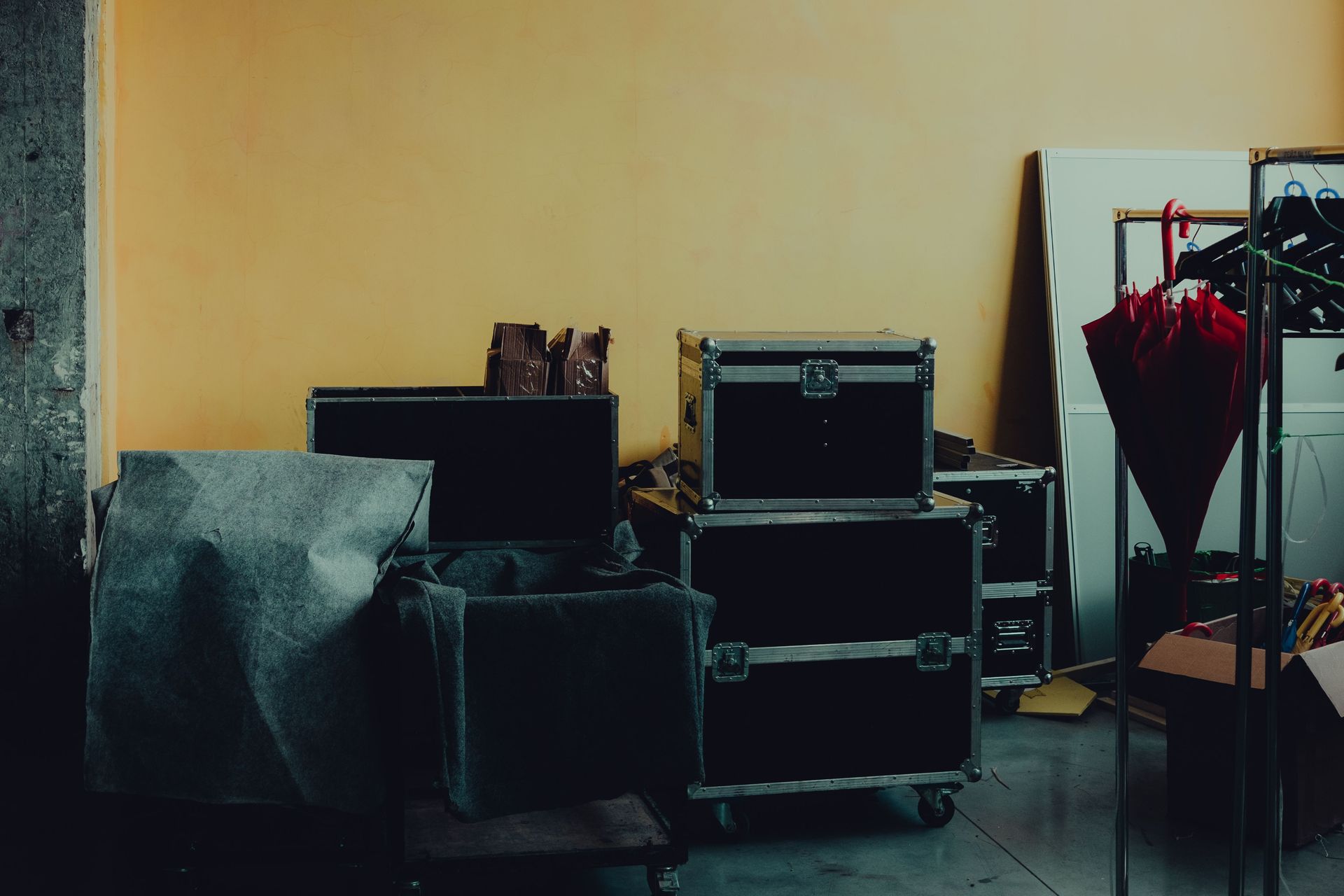 Many boxes and huge iron cases near umbrella placed in room with yellow walls